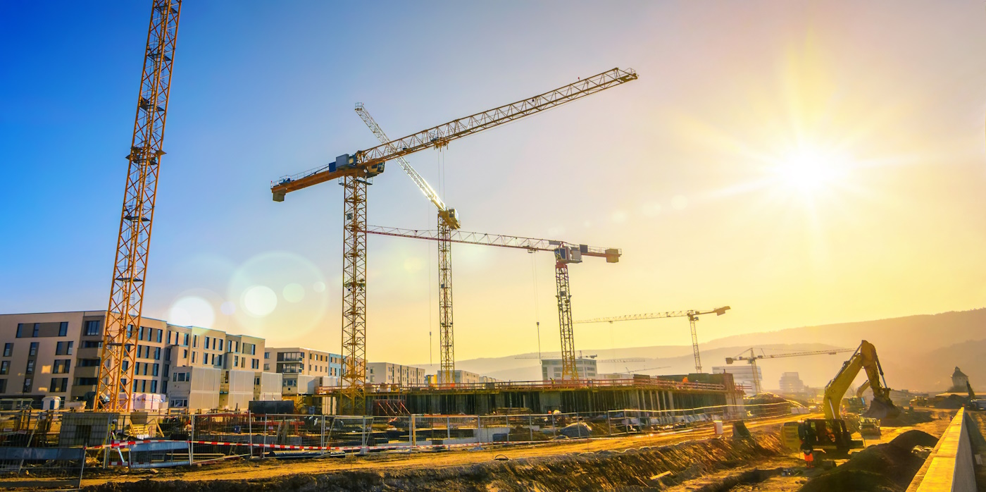 Large construction site including several cranes working on a building complex, with clear blue sky and the sun